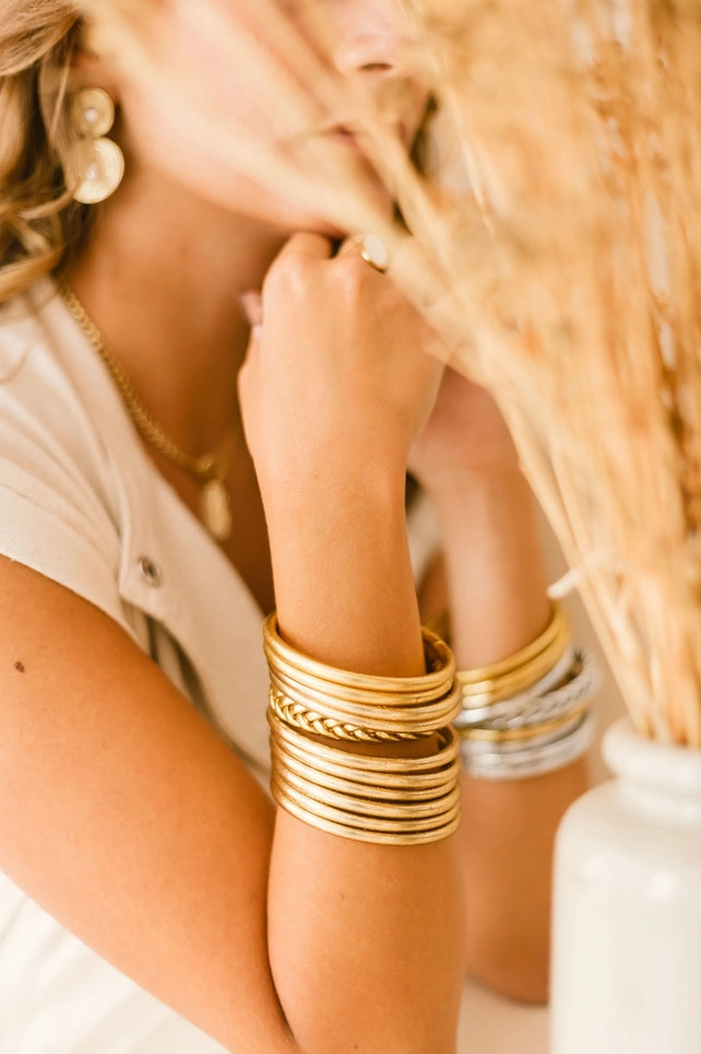 Kvinde med flere guld- og sølvfarvede Mantra-armbånd samlet omkring håndleddene.